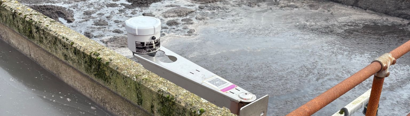 Een radarniveausensor uit de VEGAPULS Air-serie op een beugel boven het slibopvangbekken.